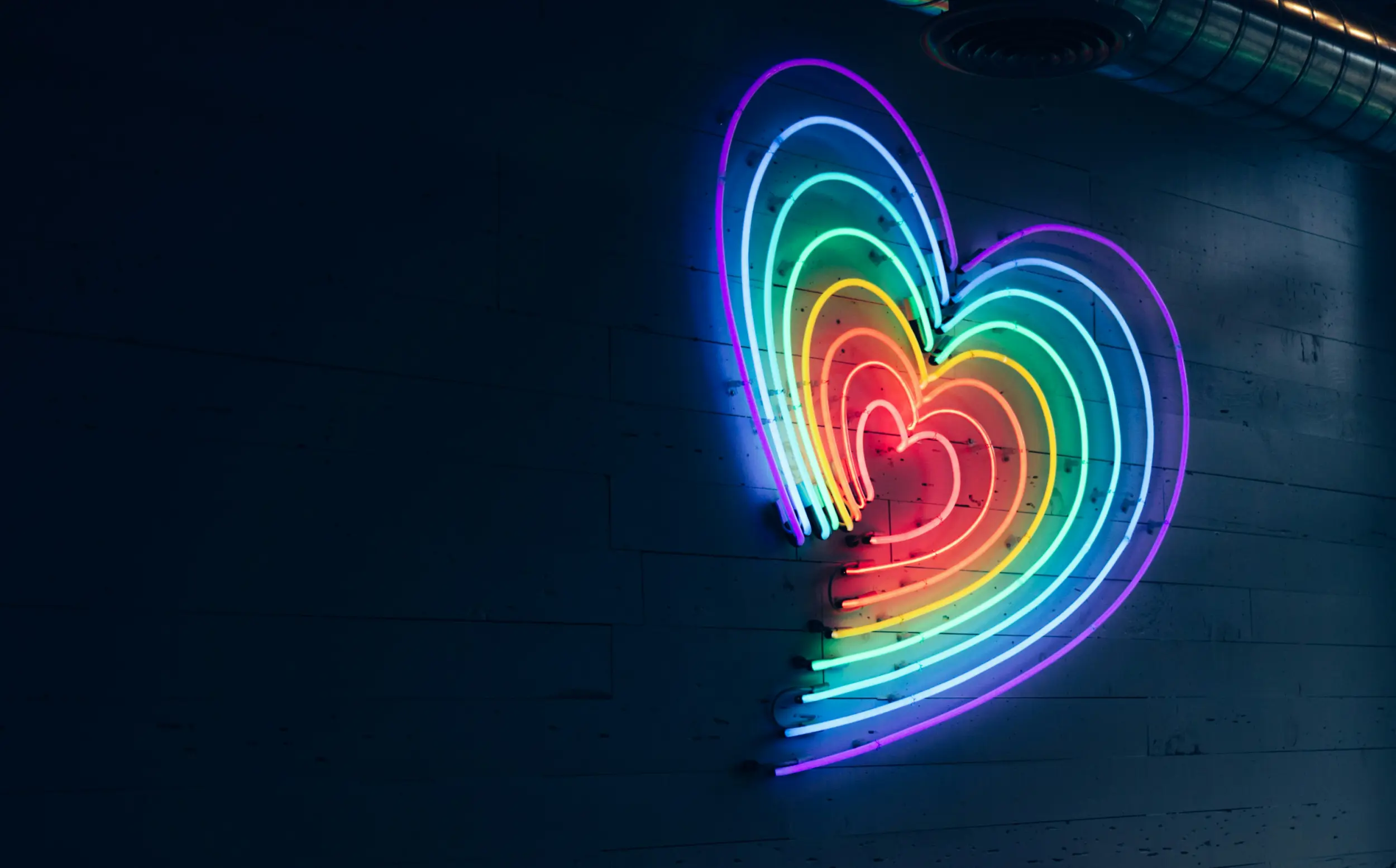 Photo of a rainbow heart with each color made of a neon light.